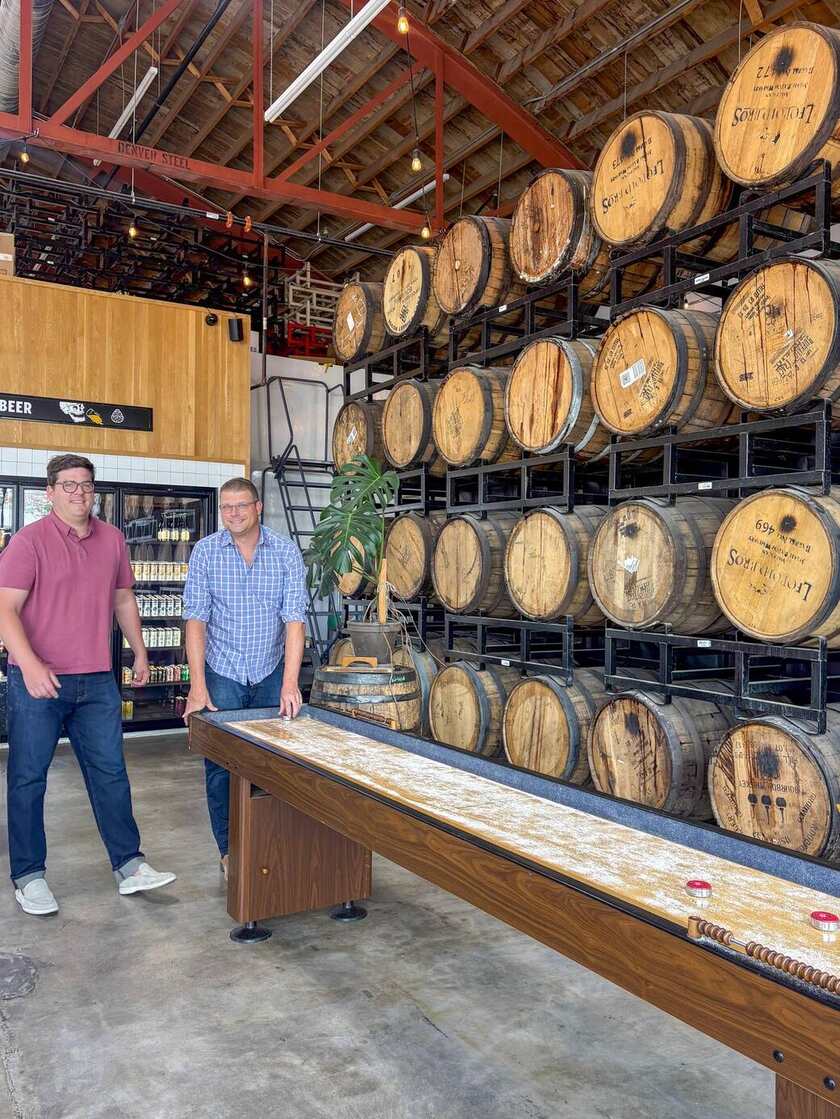 Two members of the Jade Real Estate team playing shuffleboard on a team night at a Denver brewery, with a wall of whiskey barrels behind them.